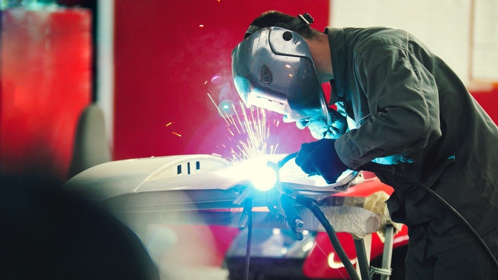 Welding industrial: worker in helmet repair detail in car auto service - blue sparklers