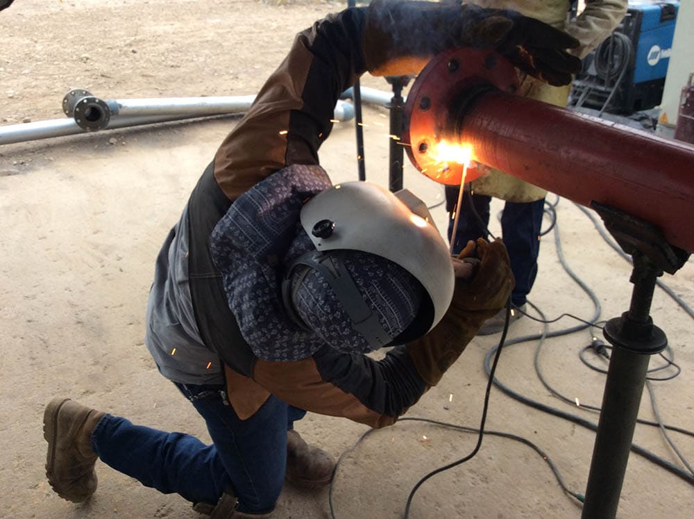 man welding a metal tube placed on a weld positioner