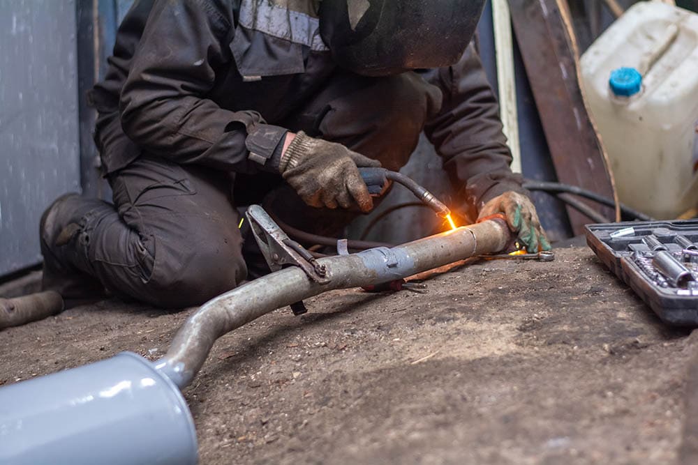 man welding a muffler in car workshop